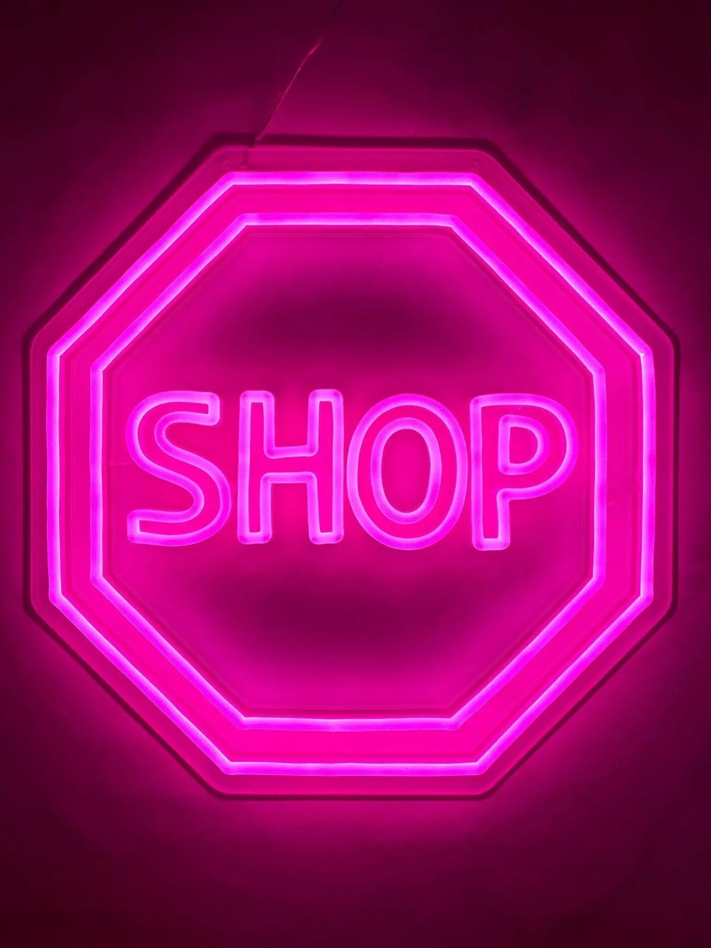 Custom LED neon pink lighted shop stop sign on a wall.