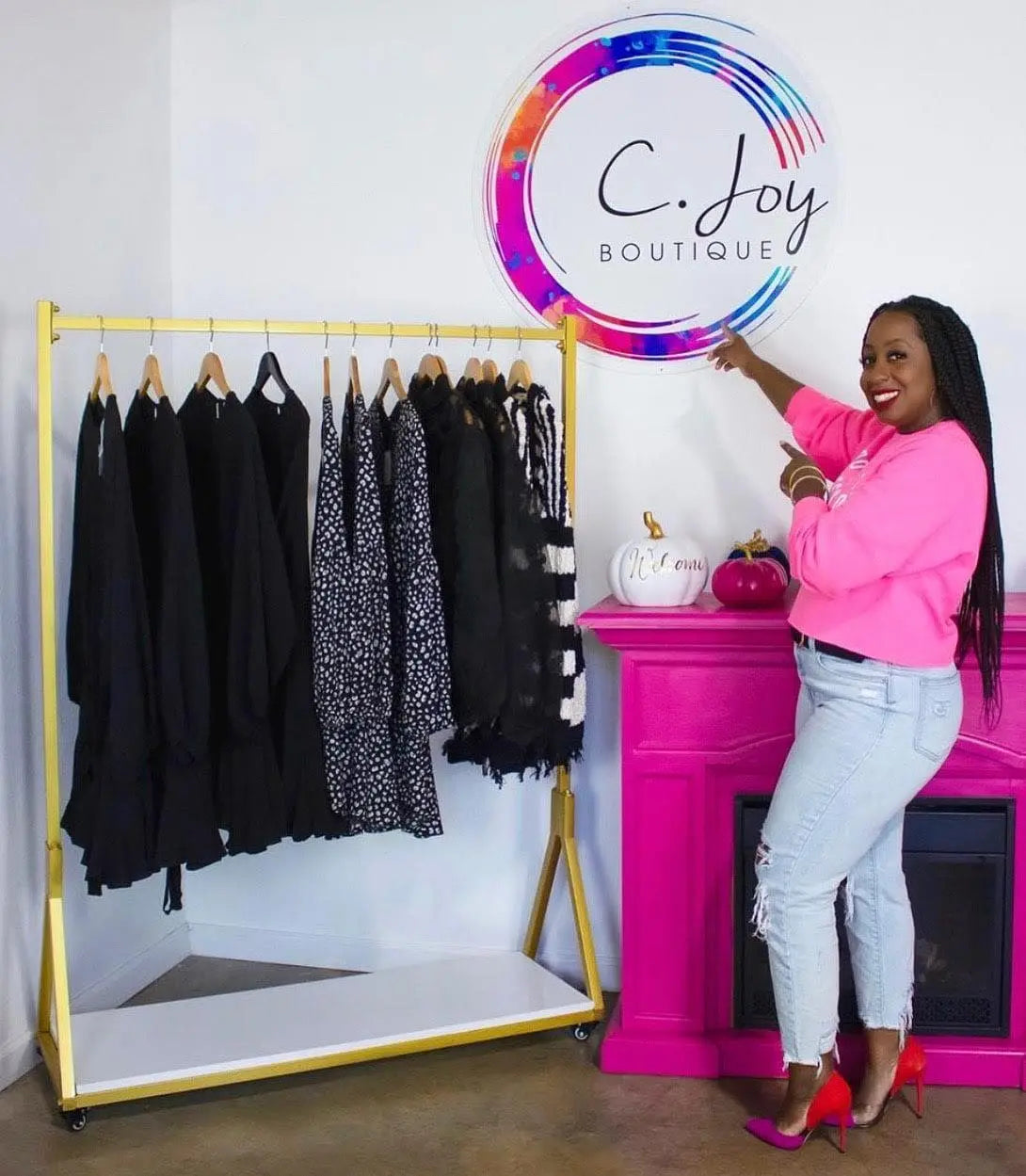 Female business owner smiling and pointing to her business logo sign in her boutique store.