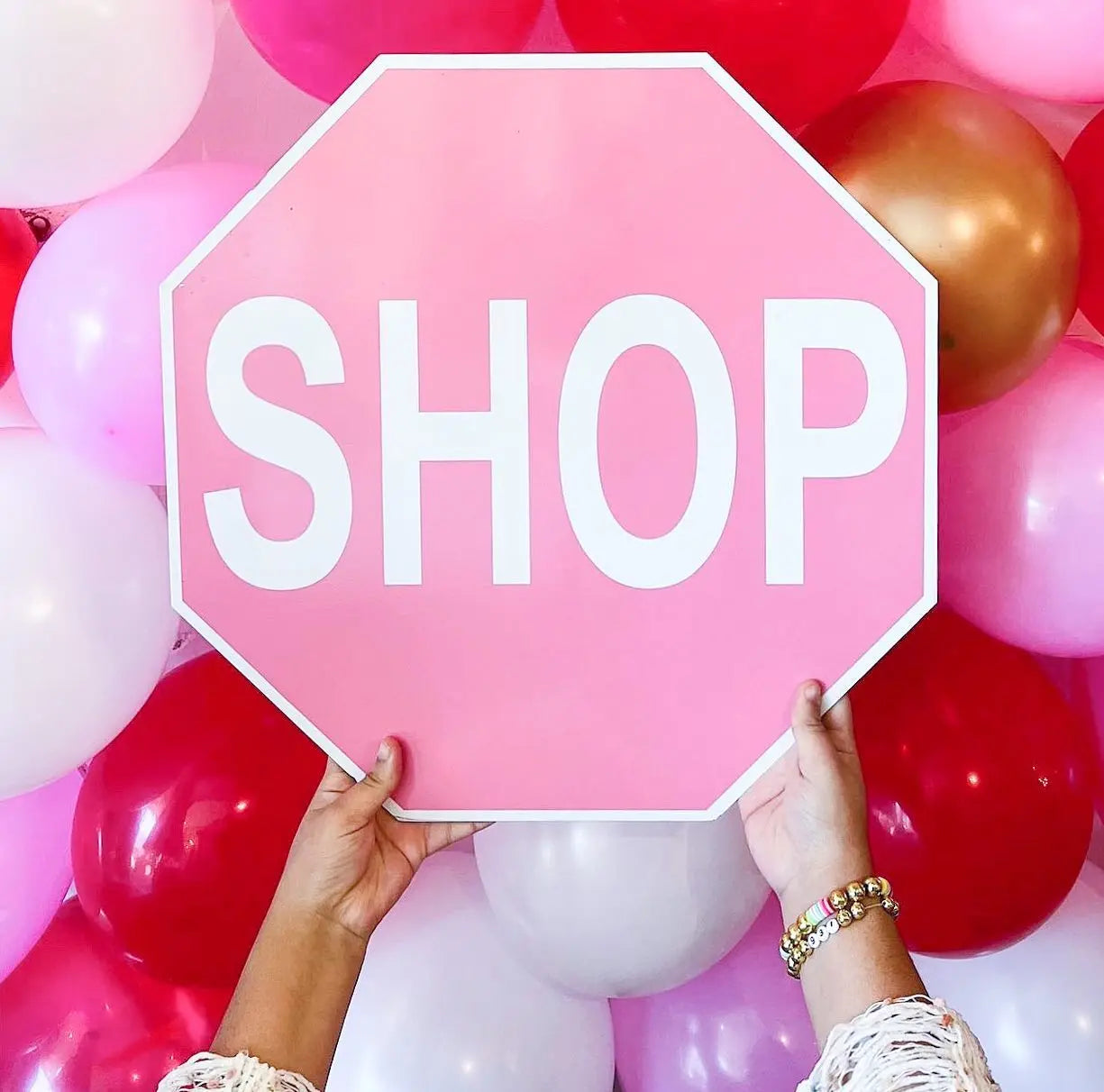 Pink shop stop sign being held in front of colorful ballons.