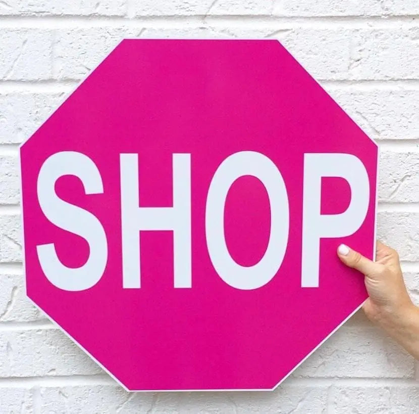 Hot pink shop stop sign in front of white brick wall.