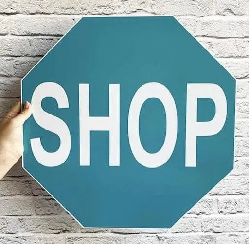 Aqua blue shop stop sign in front of white brick wall.